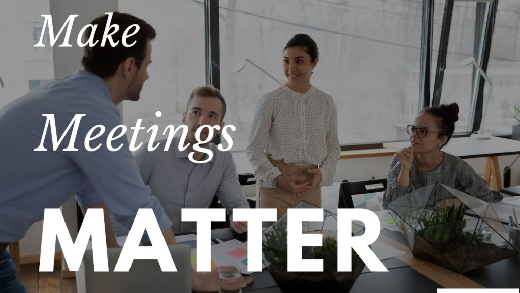 A man in a dress shirt stands over a table while three coworkers listen attentively. Text says: Make meetings matter.
